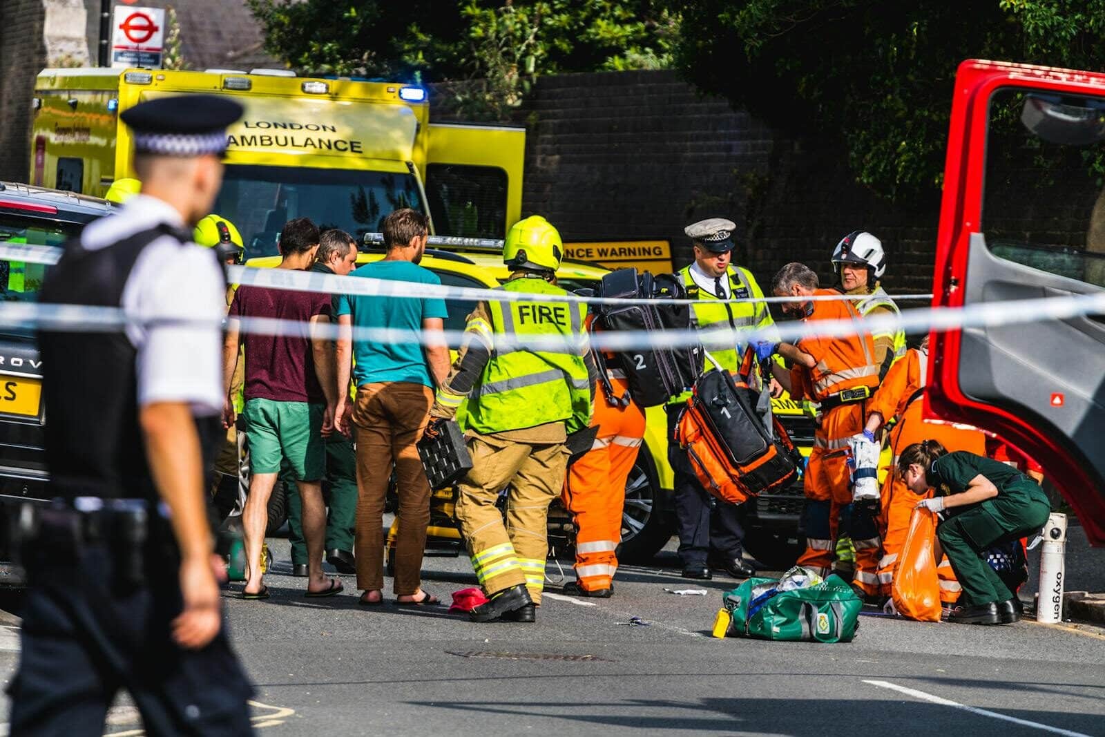 Emergency responders assisting at a street accident in London with visible metro station sign.