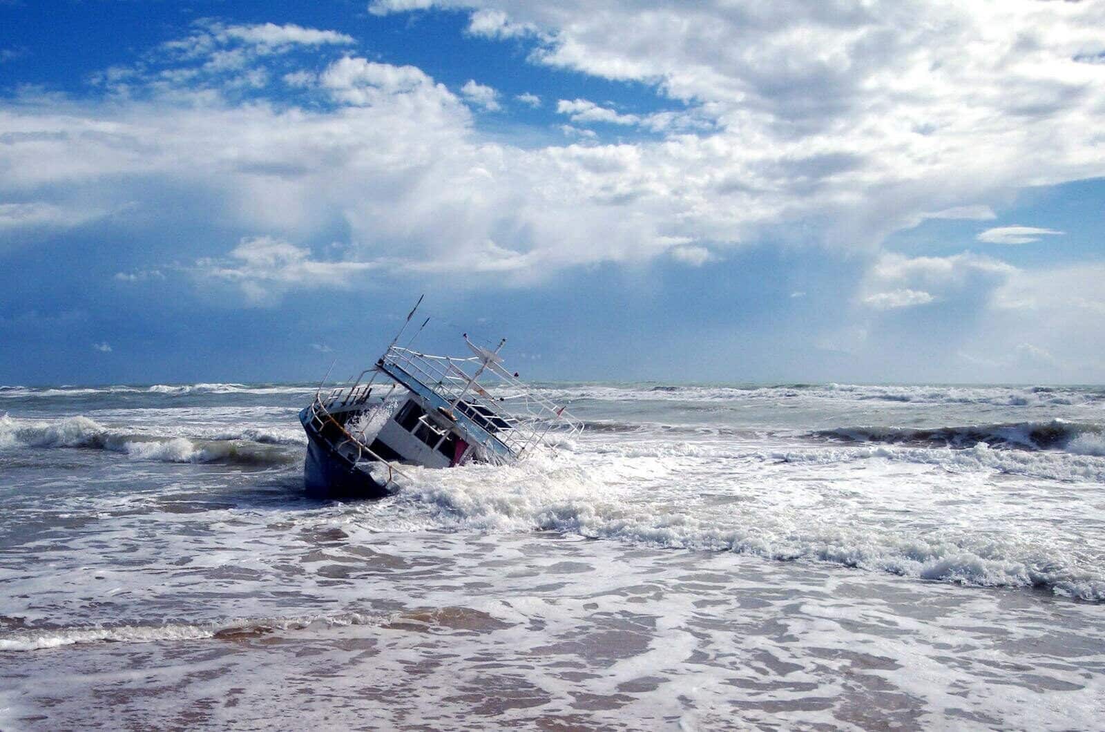 Dramatic scene of a shipwrecked boat on a stormy seashore with crashing waves and cloudy skies.