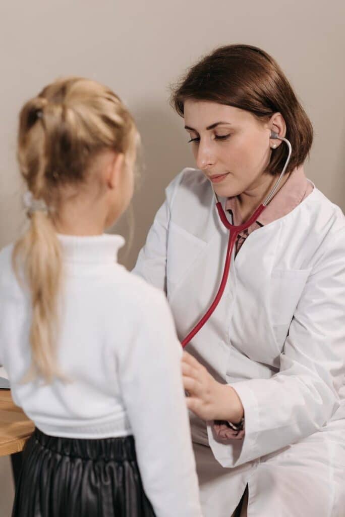 Current image: A female doctor examining a child with a stethoscope during a pediatric check-up in a clinic.