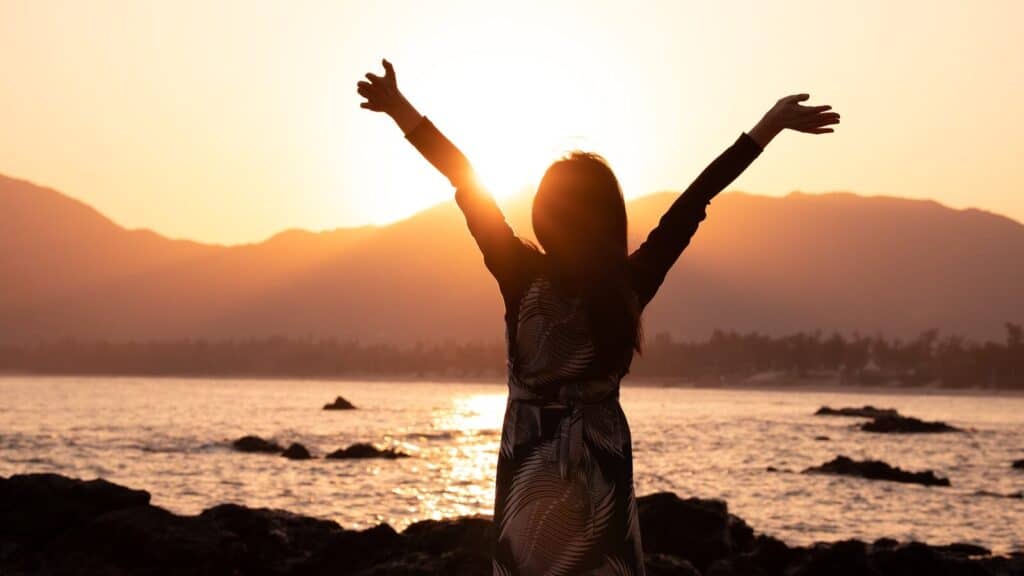 Current image: a woman standing on a beach with her arms outstretched